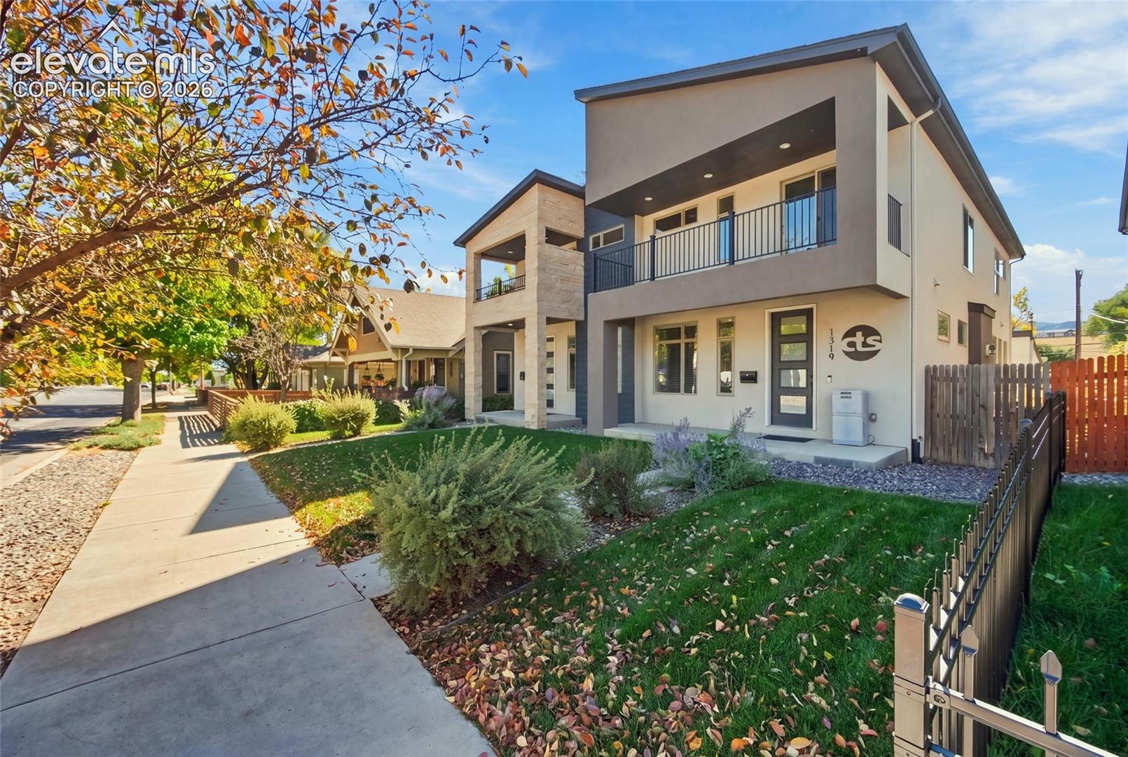 Contemporary two-story exterior featuring a mix of stucco and stone-finish siding, a second-story balcony with metal railing, and a covered front entryway