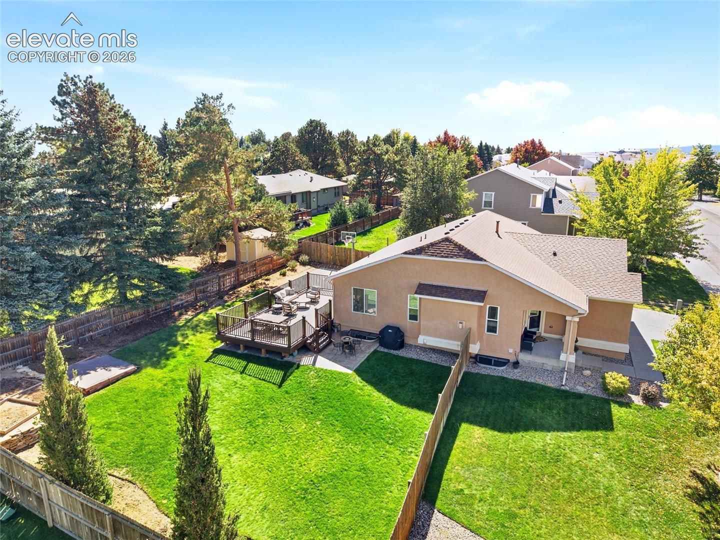 Expansive backyard featuring a manicured lawn, a multi-level wood deck, a covered patio, mature trees, and privacy fencing
