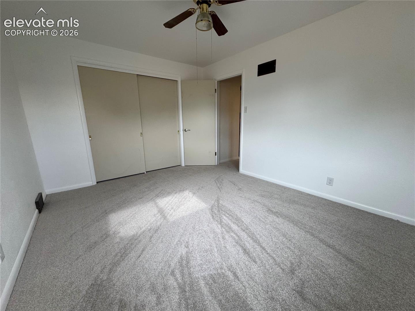 Neutral-toned wall-to-wall carpeting, ceiling fan with integrated lighting, and dual-panel sliding closet doors