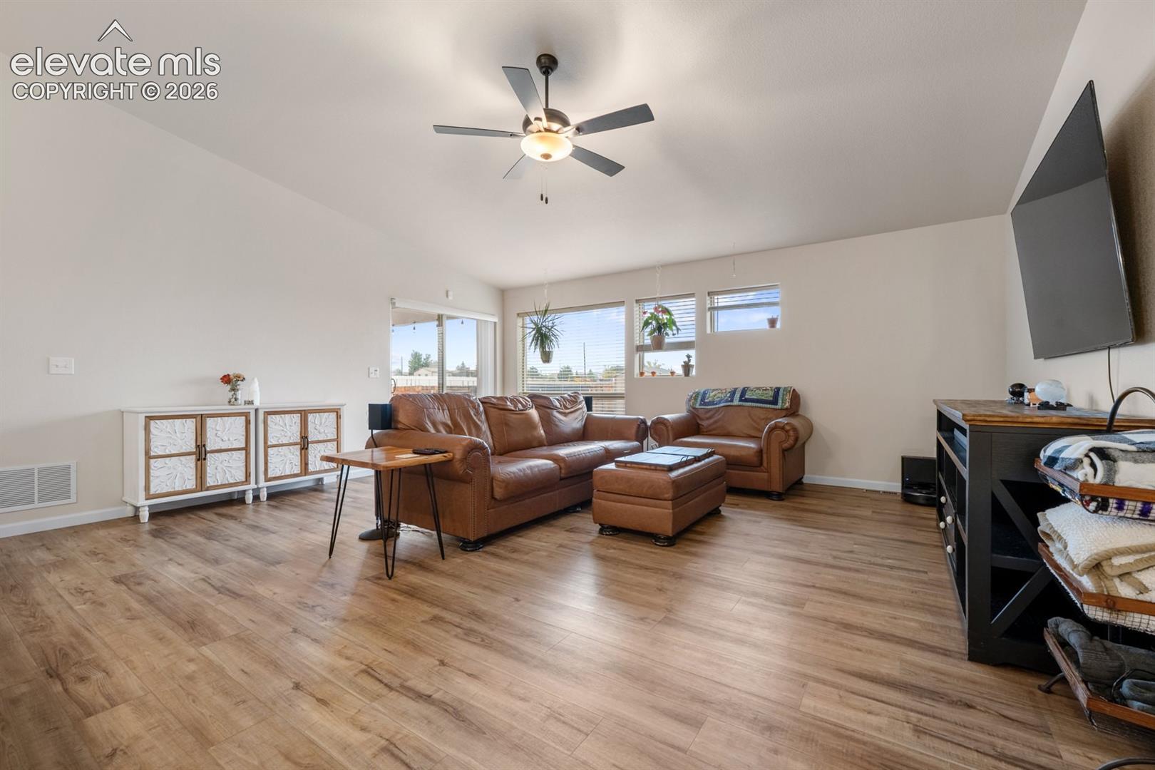 Living area featuring vaulted ceilings, wood-finish flooring, and a ceiling fan with integrated lighting