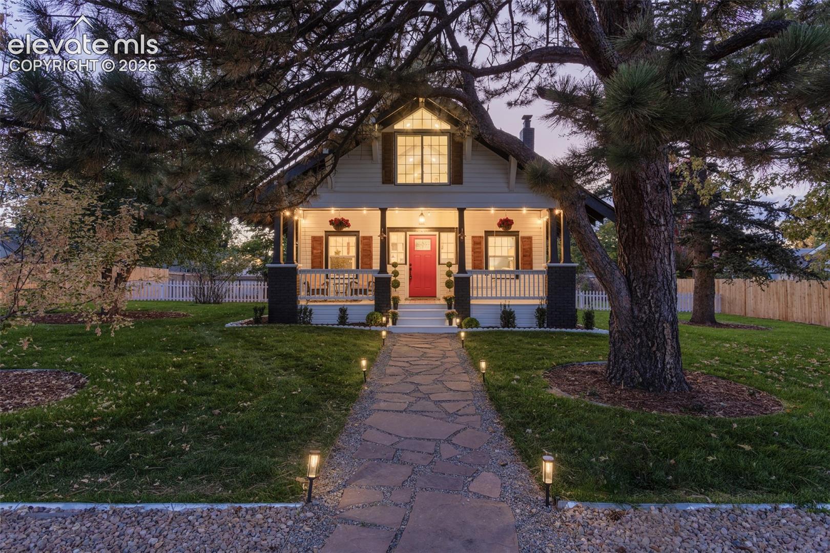 Charming home exterior featuring a red front door, covered porch, and white picket fence