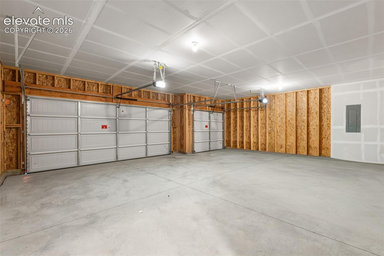 Three-car garage featuring a concrete floor, two automatic overhead door openers, and exposed structural wood-stud wall framing