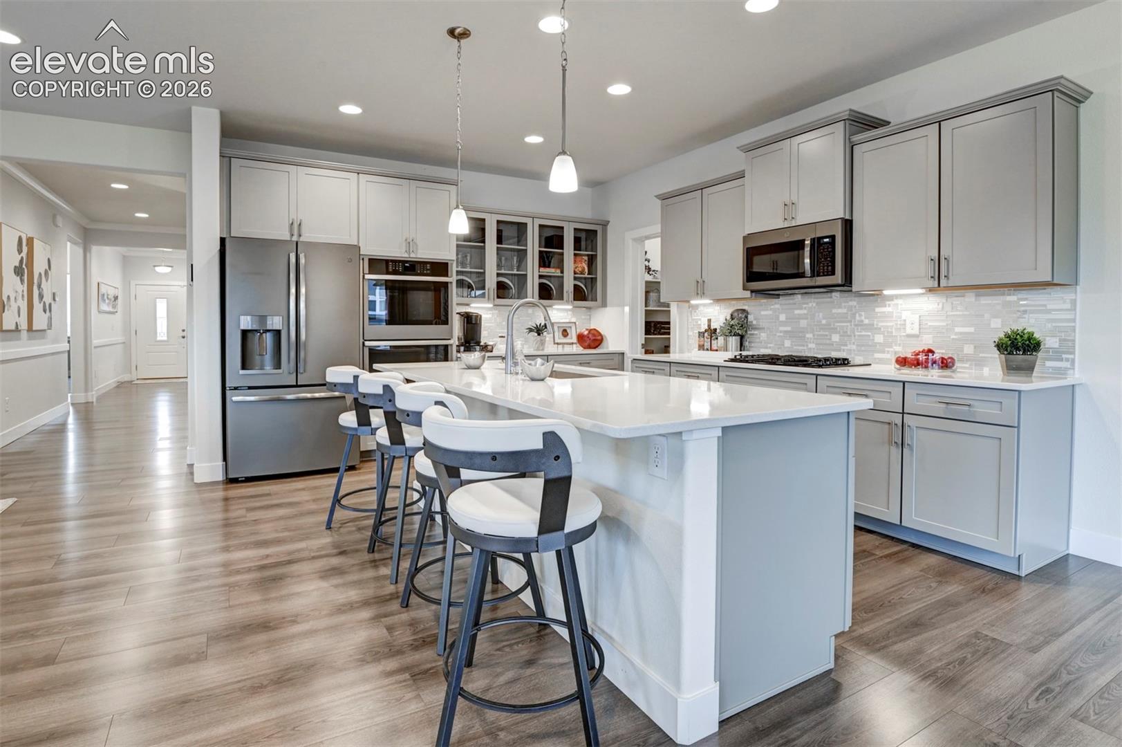 Kitchen with wood-finish flooring, white quartz countertops, stainless steel appliances, and grey cabinetry, featuring a central island with pendant lighting