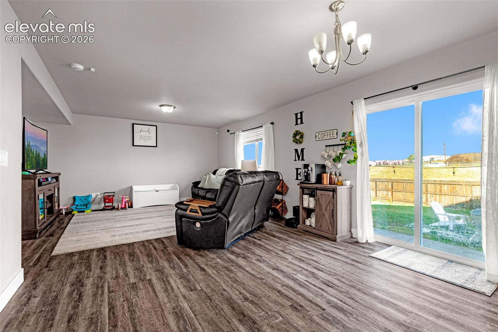 Spacious living area featuring wood-finish flooring, light grey walls, and a five-light chandelier
