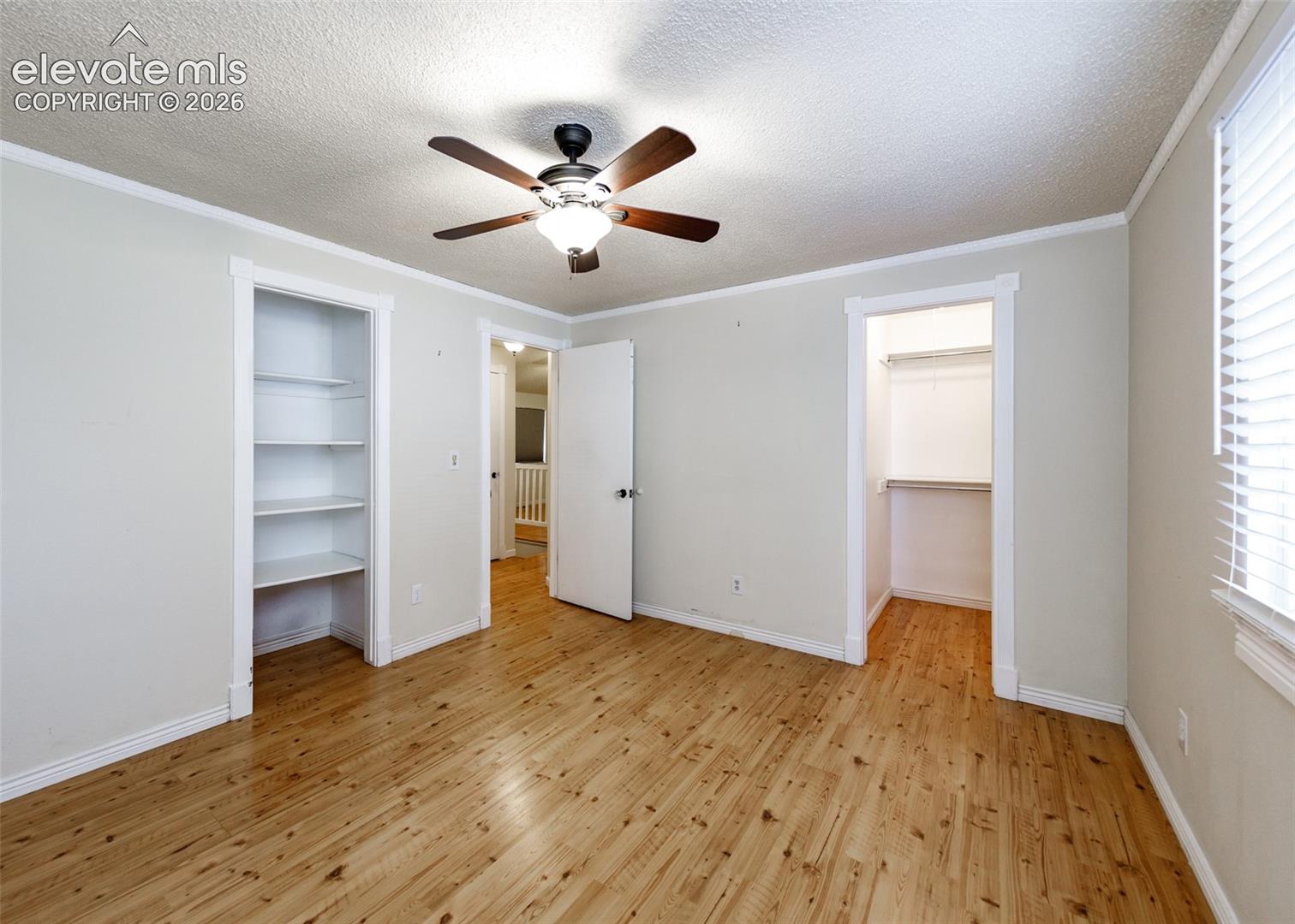 Room featuring wood-finish flooring, a ceiling fan with integrated lighting, built-in shelving, and a closet with a fixed hanging rod