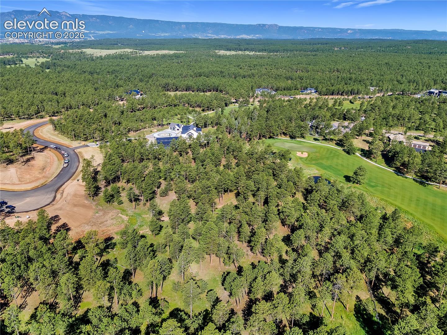 Aerial perspective of a multi-acre wooded lot featuring mature pine trees, paved access road, and proximity to an expansive golf course with mountain backdrops