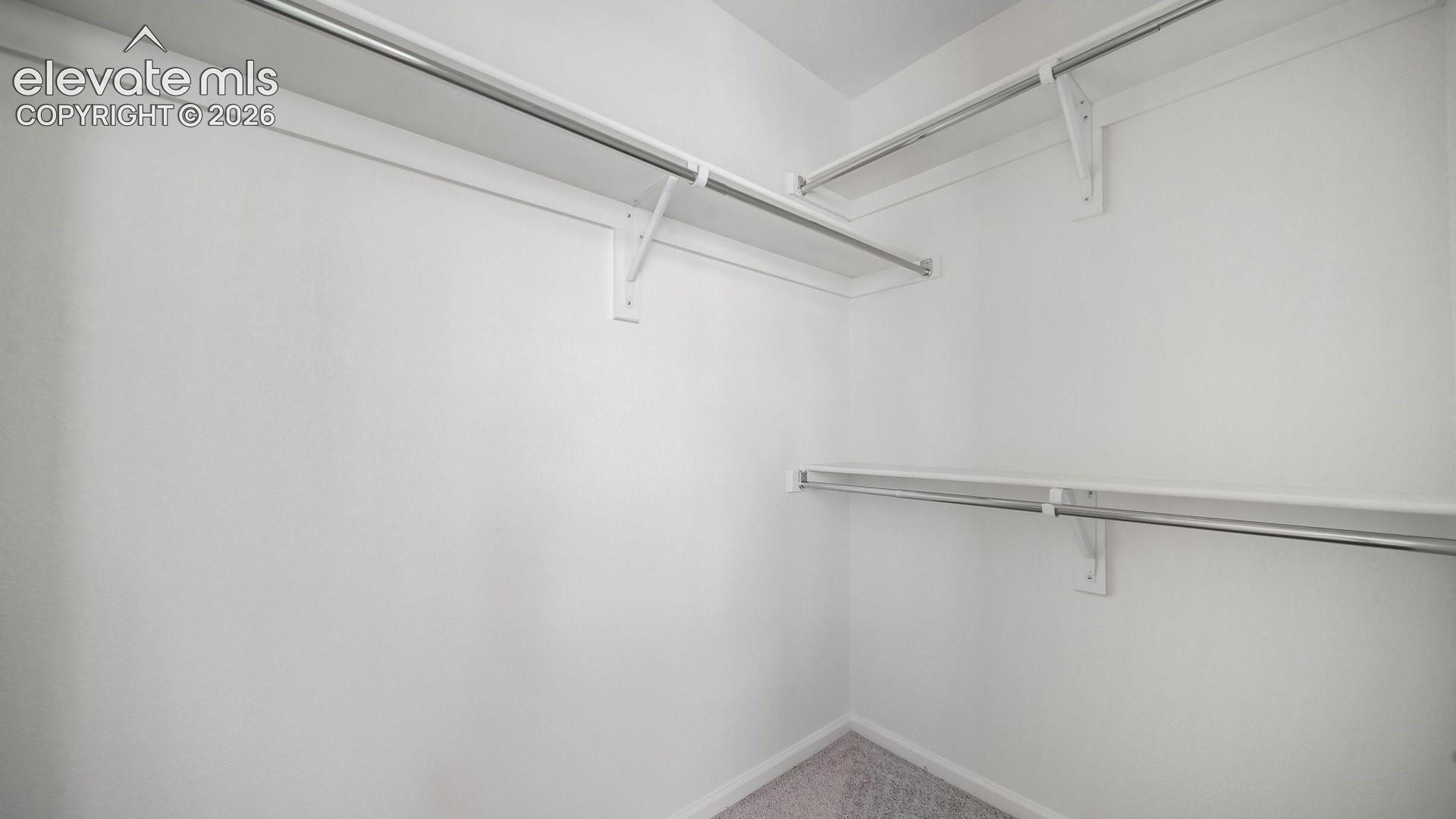 Walk-in closet featuring multi-level metal garment rods and white built-in shelving
*photos of a model home*