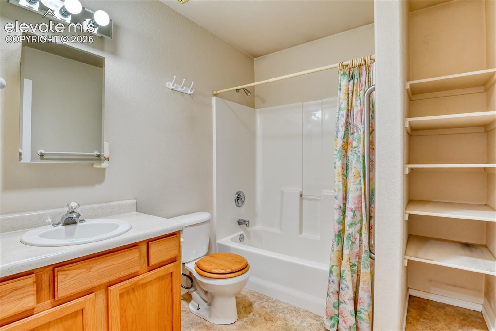 Bathroom featuring a wood-finish vanity with a molded countertop, a built-in recessed shelving unit, a combination tub and shower with a molded surround, and a wall-mounted light fixture