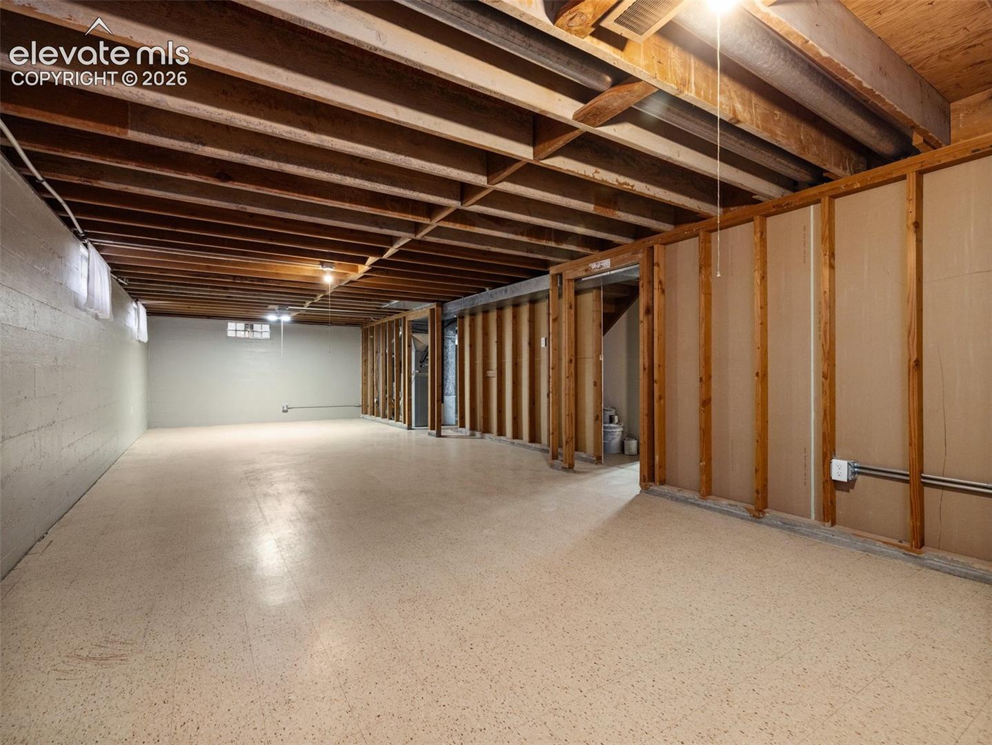 Spacious unfinished lower level with exposed wood joists and concrete block walls