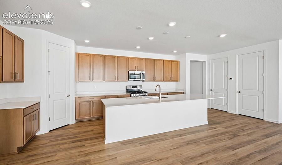 Kitchen featuring wood-finish cabinetry, a central island with a solid-surface countertop, recessed lighting, and wood-finish flooring