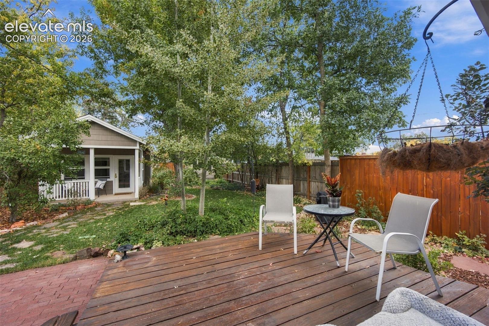 Wood-plank deck featuring a brick paver walkway, mature trees, and a wood privacy fence