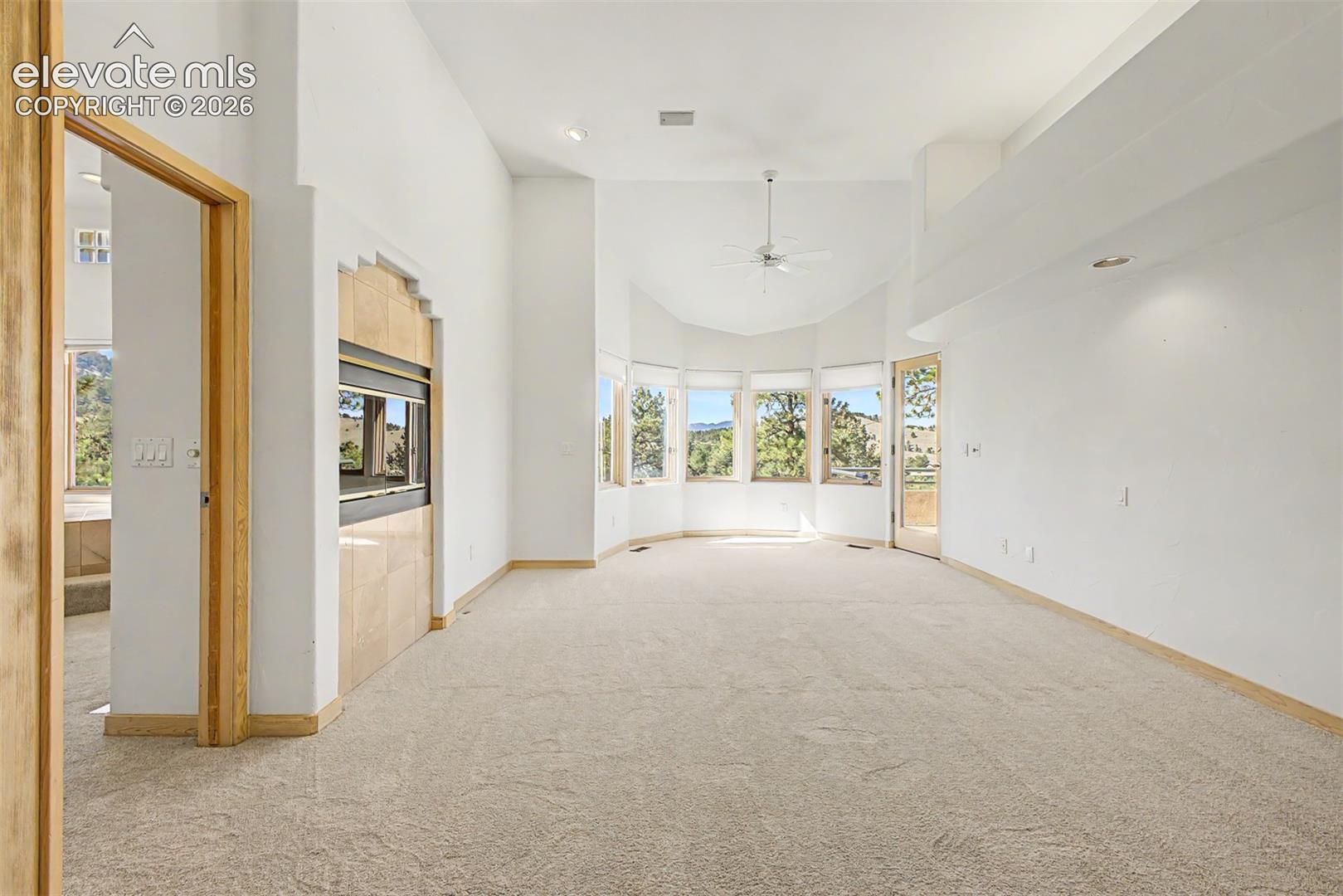Spacious room with vaulted ceilings, a built-in fireplace featuring stone-look surround, a bay window with multiple panes, recessed lighting, and a ceiling fan