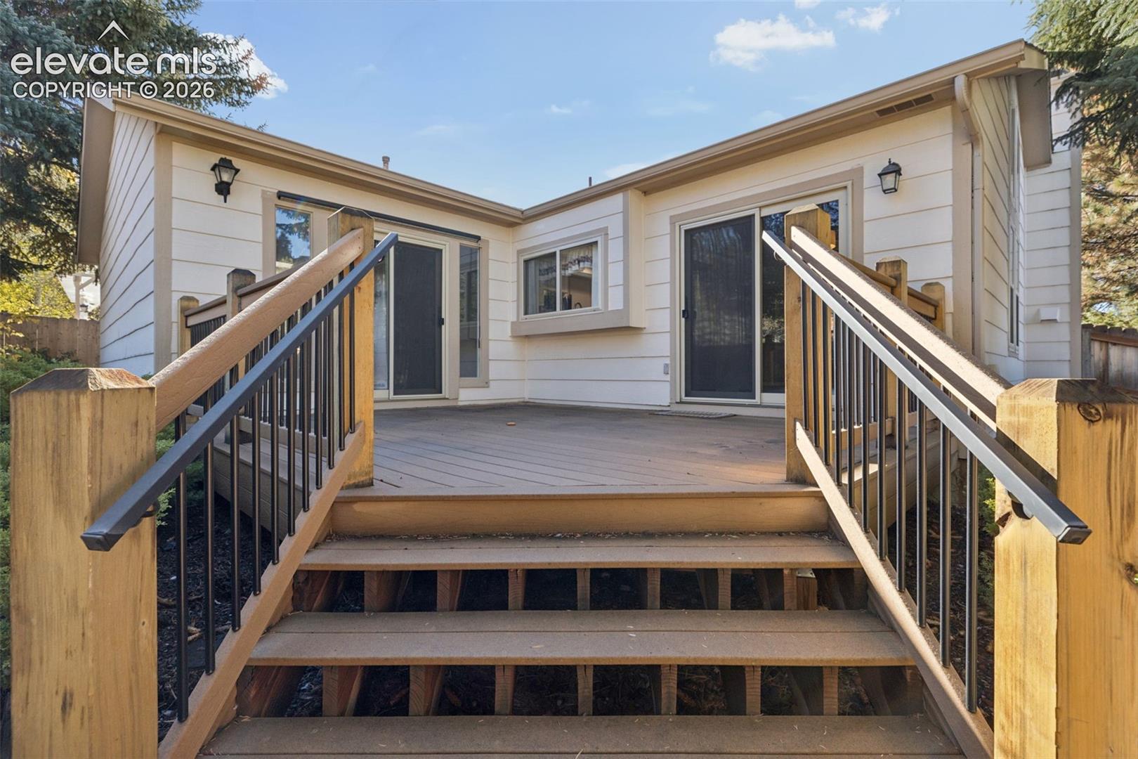 Rear exterior deck featuring wood-finish decking, black metal balusters, matching wooden handrails, and dual sliding glass doors