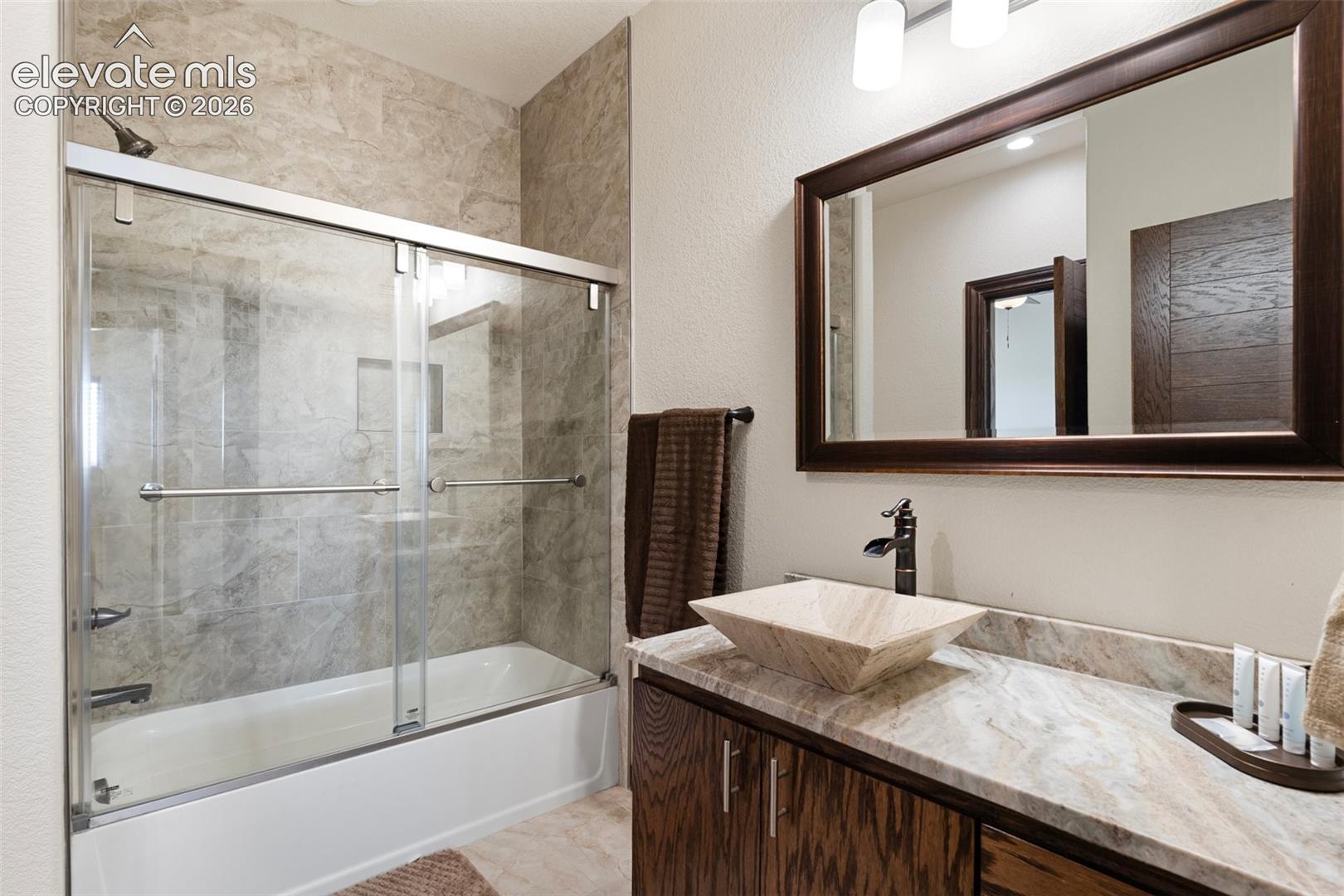 Bathroom featuring a combination tub/shower with sliding glass doors, a vanity with a vessel sink, a framed mirror, and a wood-finish cabinet