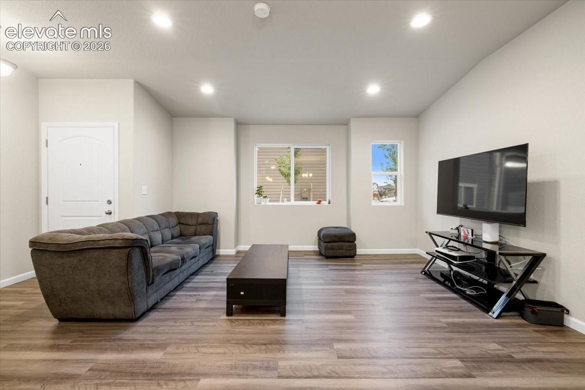 Vaulted ceiling with recessed lighting, wood-finish flooring, and white interior walls