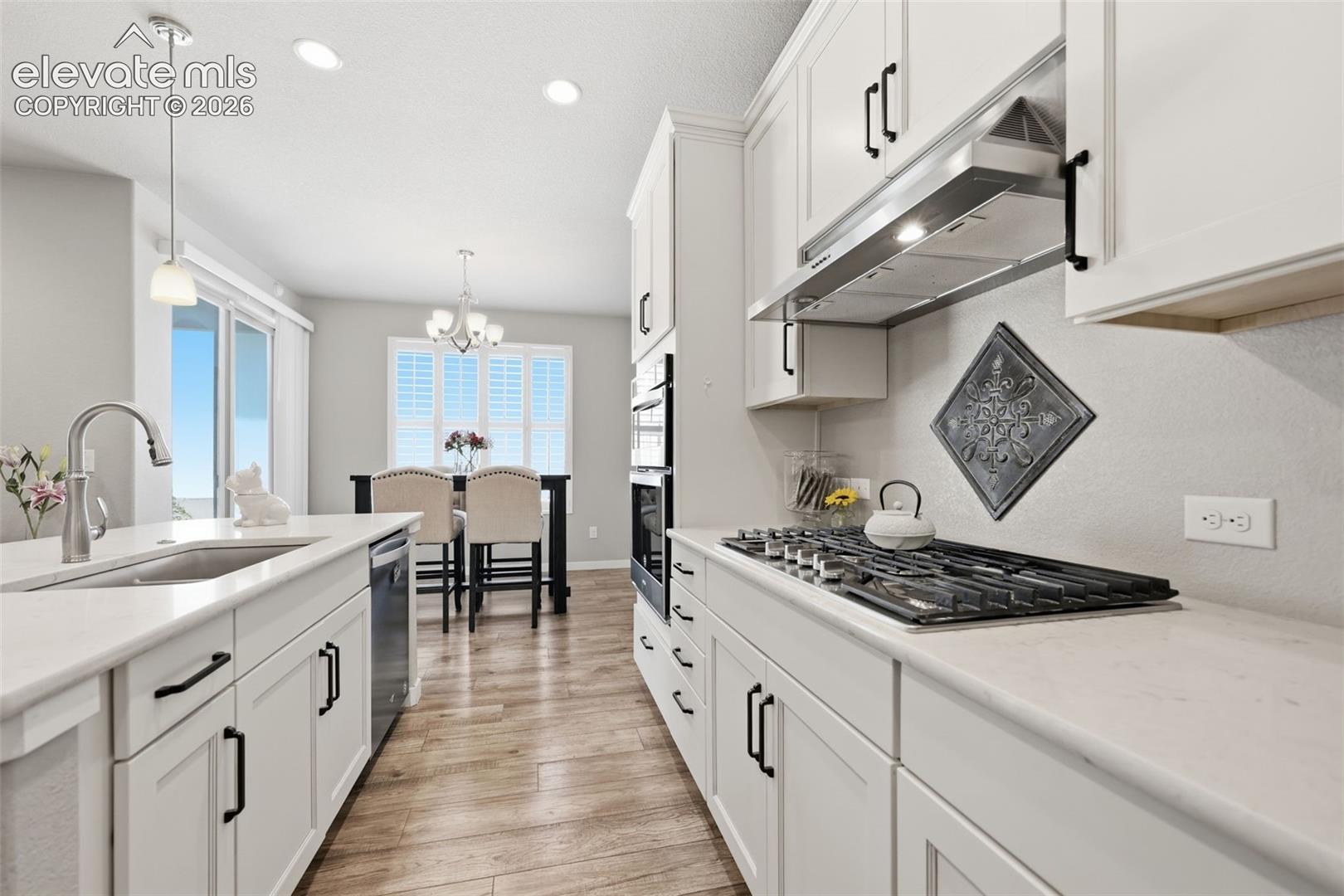 White shaker cabinetry with black hardware, light brown luxury vinyl plank flooring, stainless steel appliances, light color stone countertops, and recessed lighting.