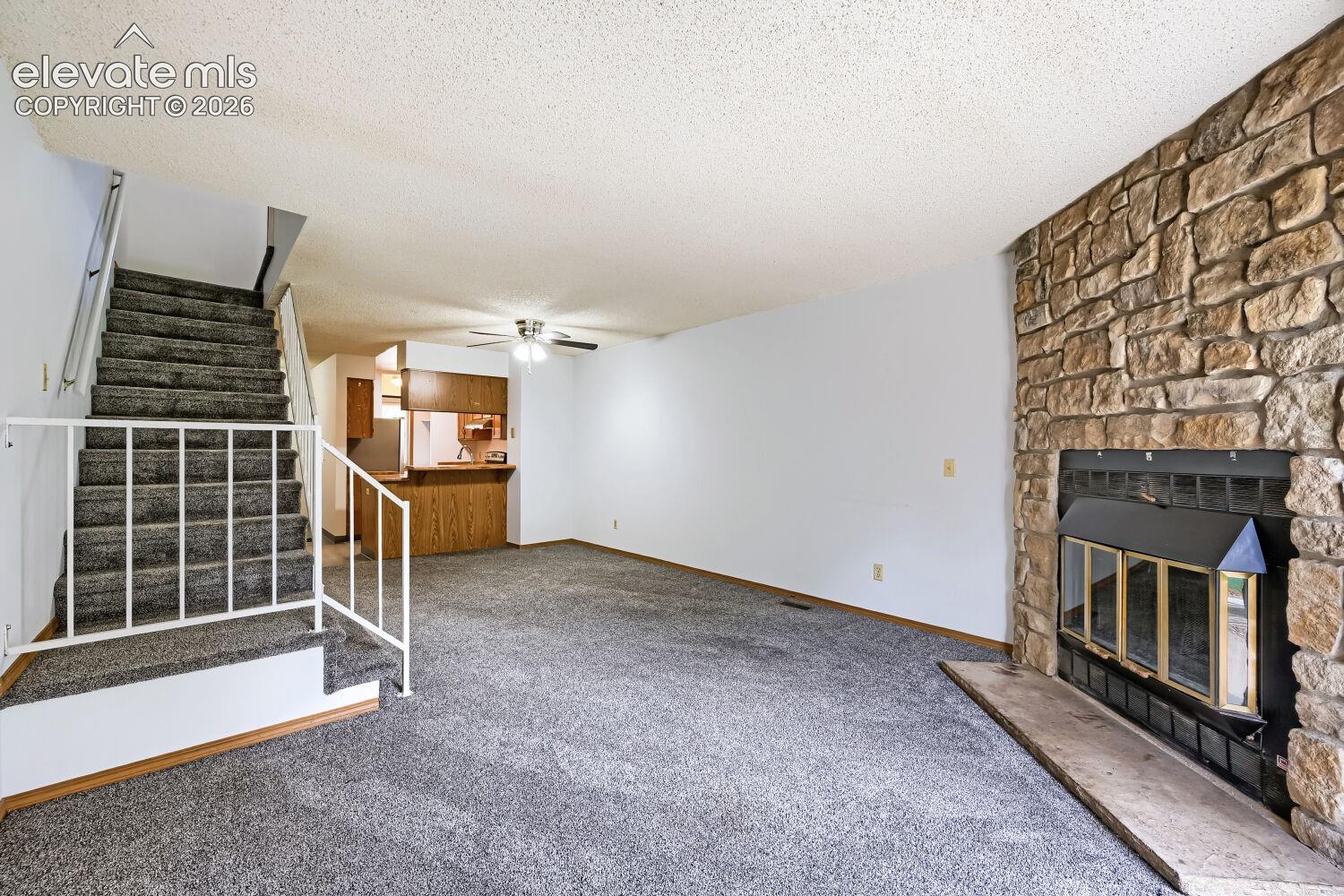 Stone-front fireplace with a black insert, open-concept living area, and a kitchen pass-through window