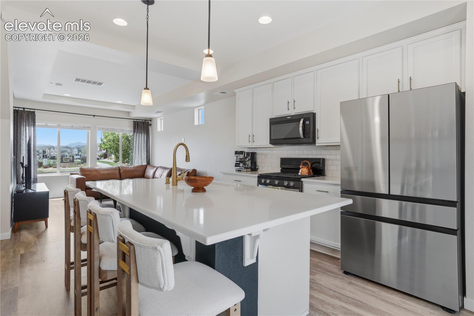 Open-concept kitchen featuring a quartz island with seating, stainless steel appliances, white shaker cabinetry, and a subway tile backsplash
