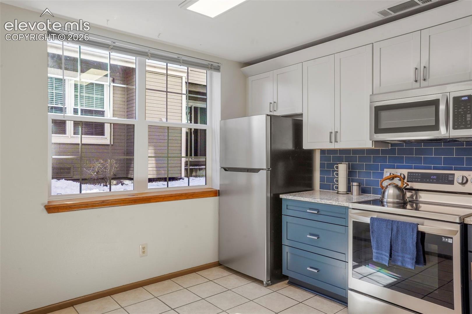 Kitchen with white cabinetry, light tile patterned floors, stainless steel appliances, and tasteful backsplash