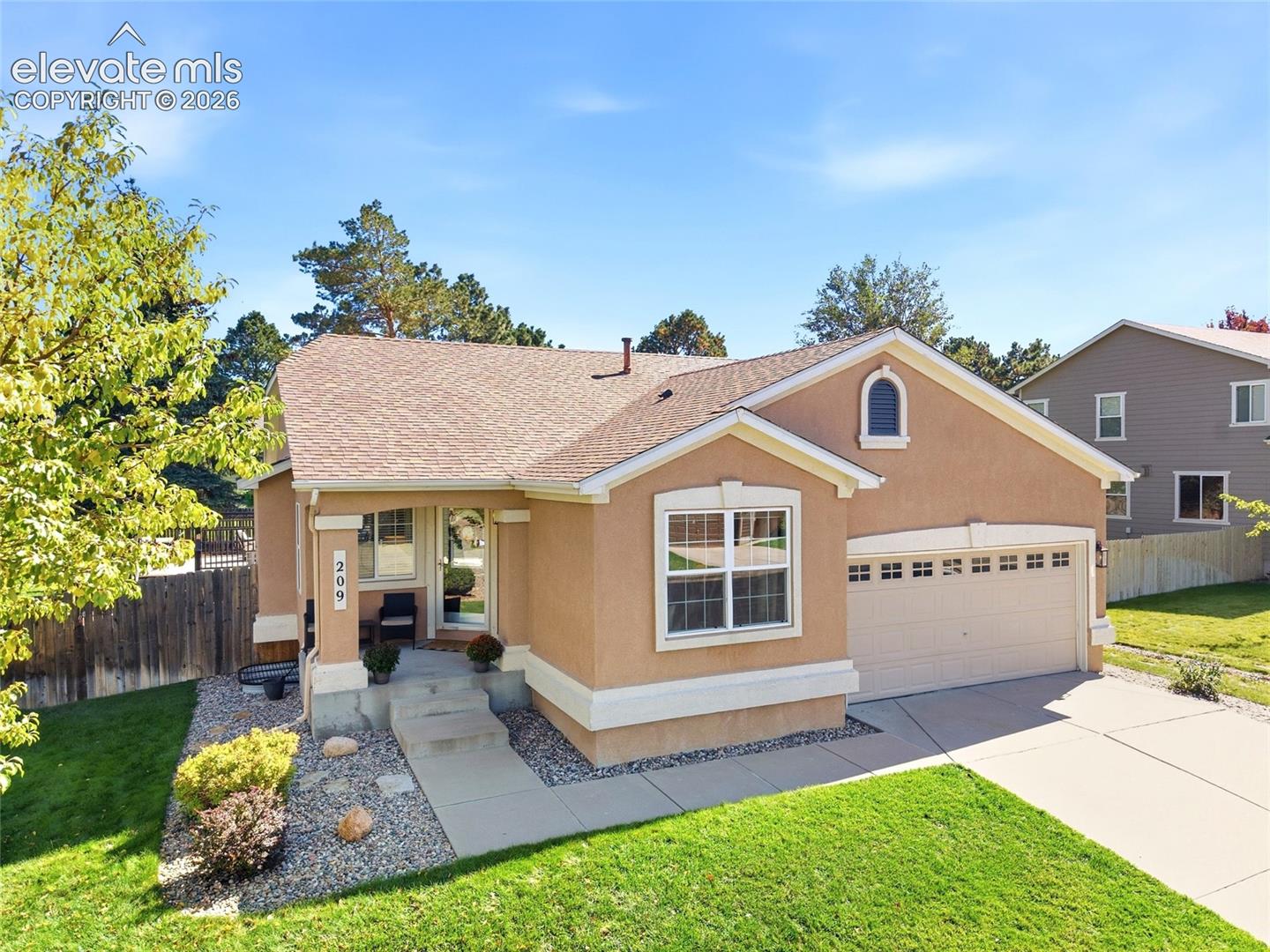 Stucco exterior with arched window accent, attached two-car garage, concrete driveway, and covered front porch with concrete steps