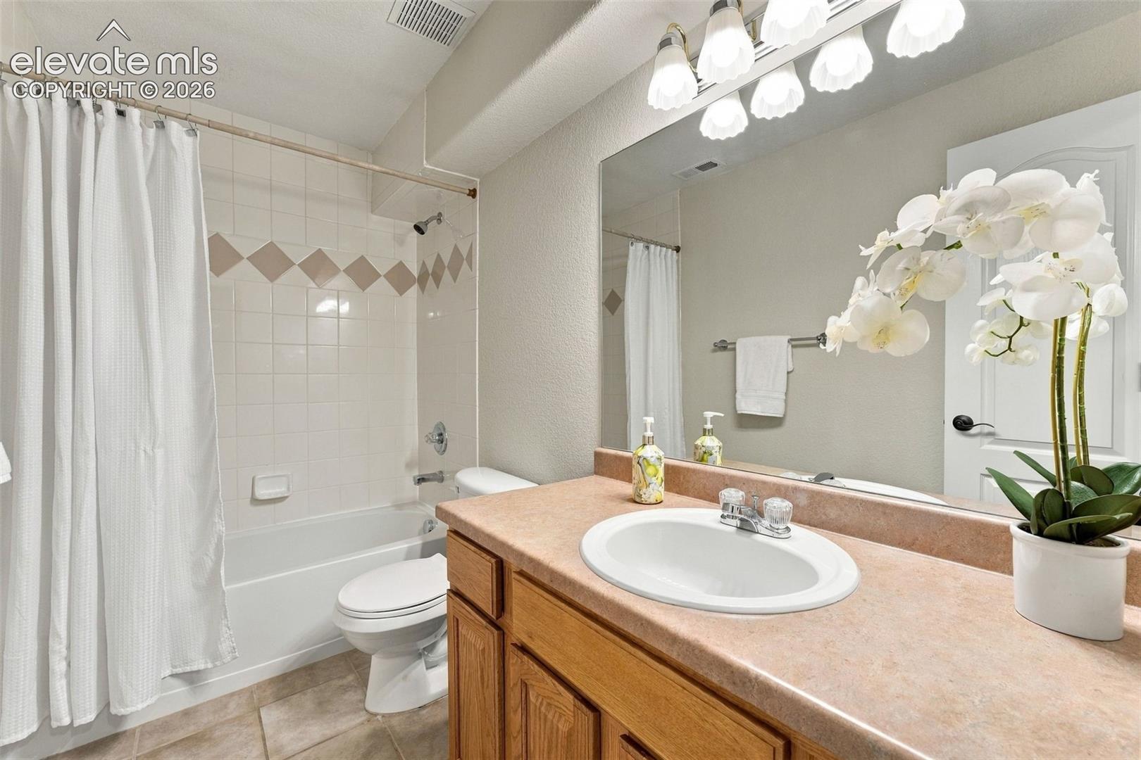 Bathroom vanity featuring wood-finish cabinetry, solid-surface countertop with an integrated oval basin, and a full-width mirror with multi-bulb light fixture