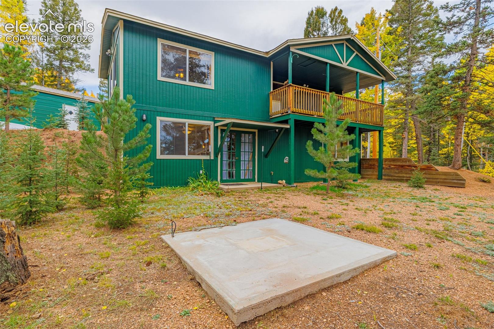 Two-story exterior featuring vertical siding, a raised wooden deck with railings, glass-panel entry doors, and a concrete ground-level pad