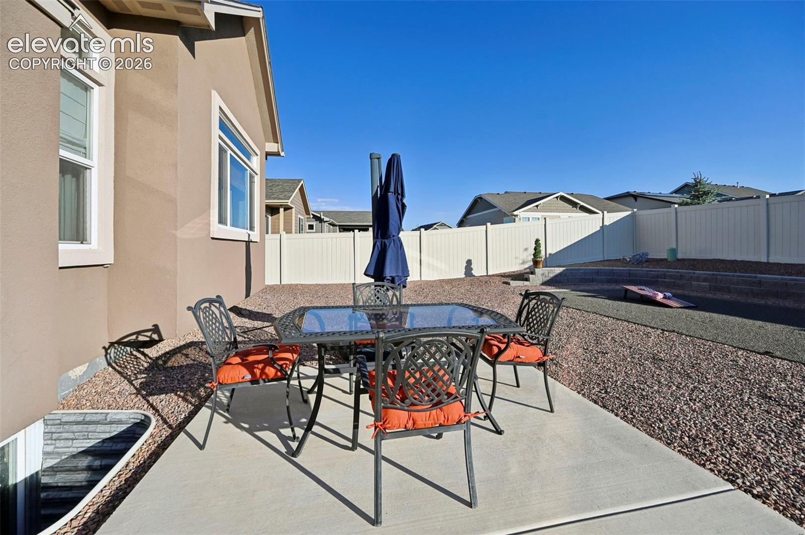 Concrete patio with a stucco exterior, surrounded by gravel landscaping and a white privacy fence