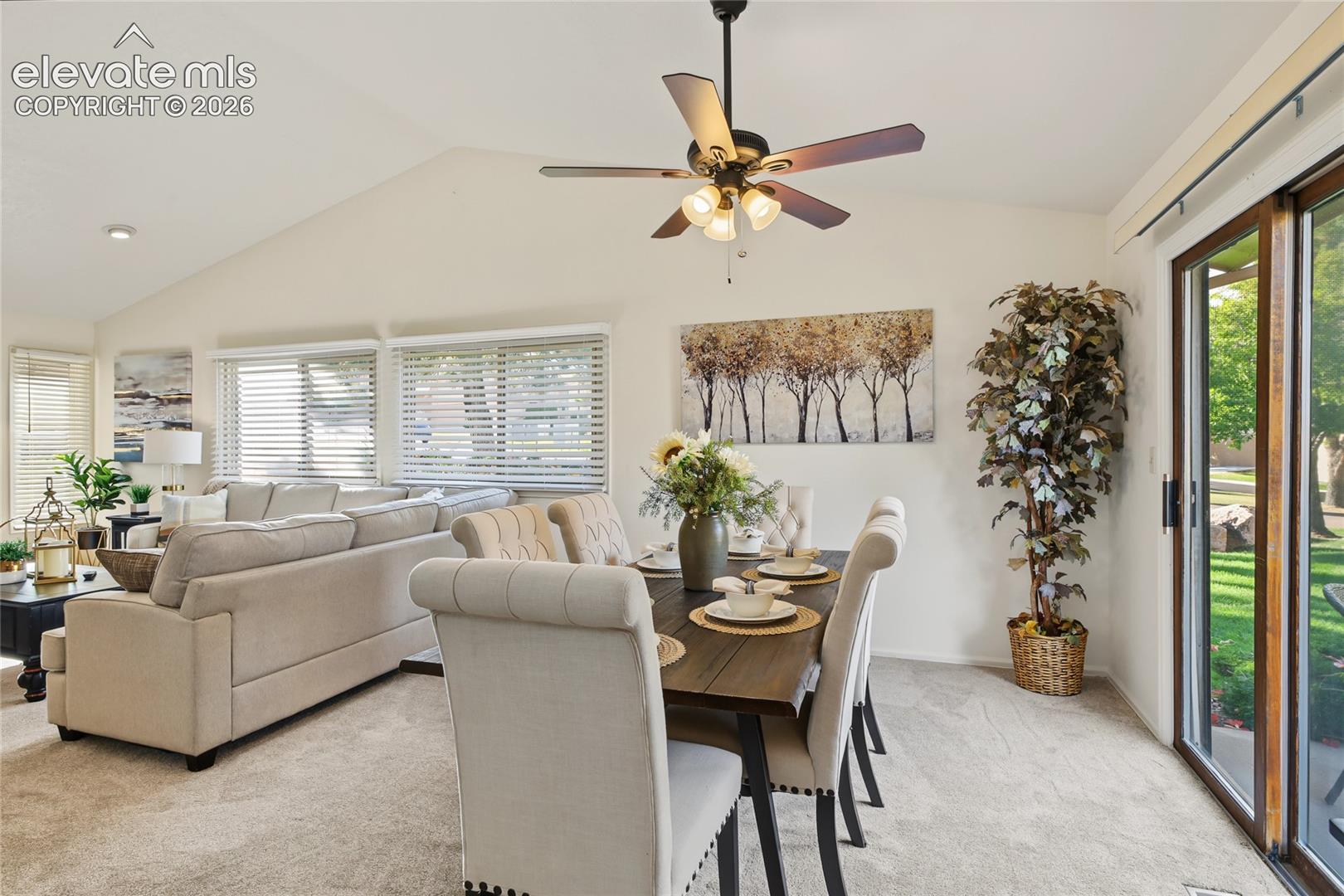 Vaulted ceilings with a ceiling fan, wall-to-wall carpeting, multiple windows with blinds, and a sliding glass door