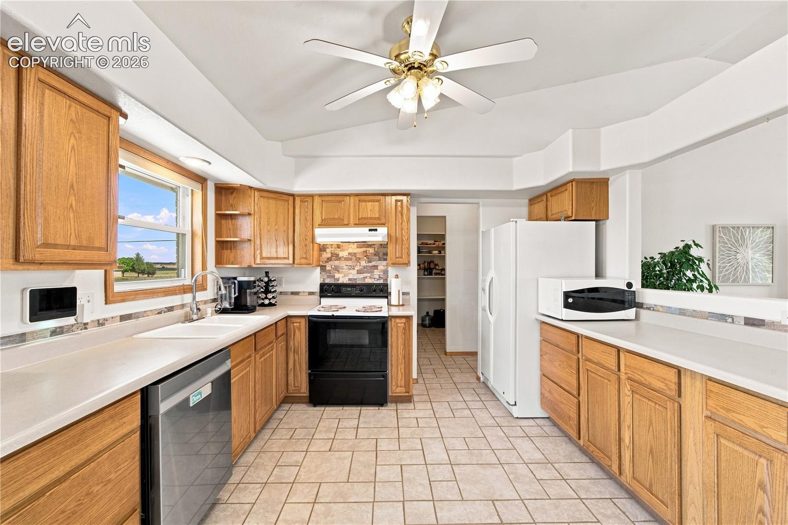Kitchen featuring wood cabinetry, light-toned countertops, tile flooring, stainless steel dishwasher, and a ceiling fan with integrated lighting