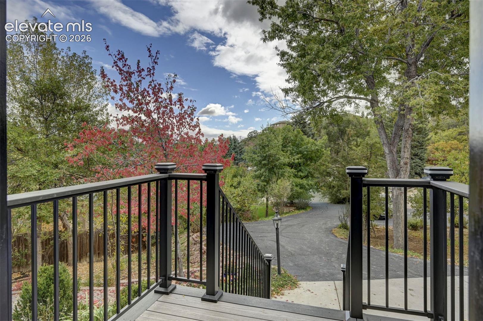 Elevated exterior deck with black metal railing, composite decking, and mature tree-lined scenery