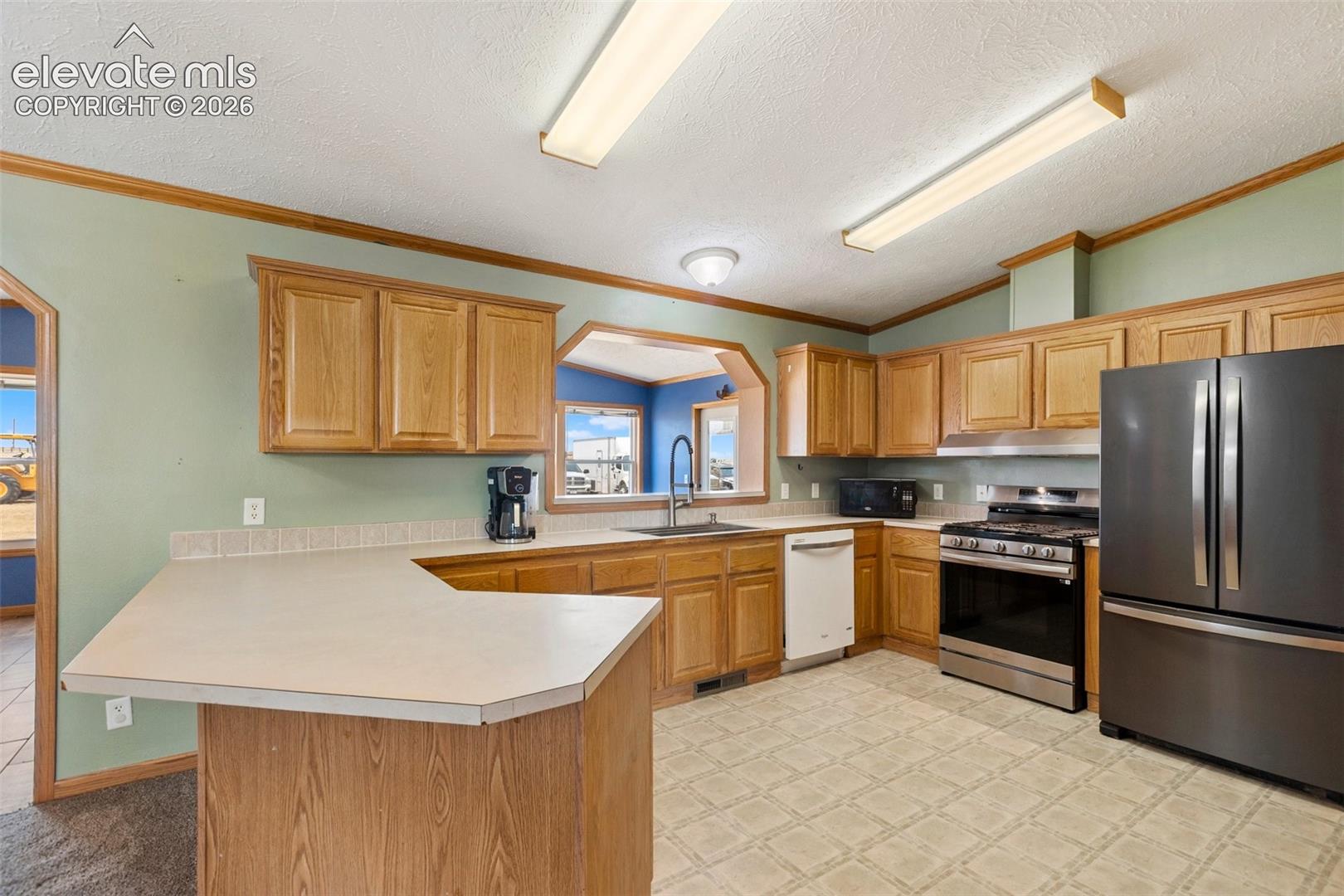 Kitchen featuring wood-finish cabinetry, a peninsula with a countertop, stainless steel appliances, and a tiled backsplash