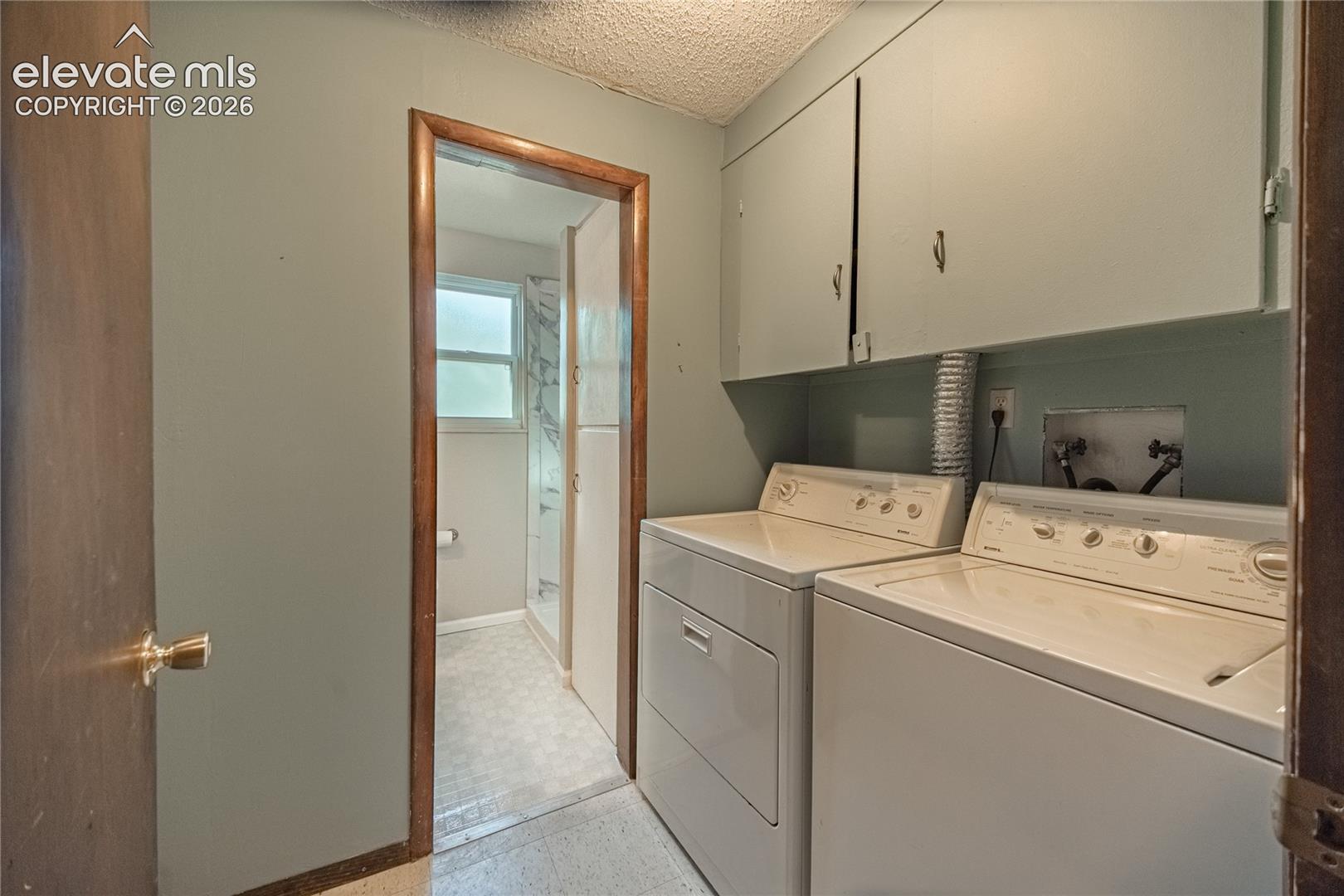 Laundry area featuring built-in overhead cabinetry and standard water hookups, providing utility space with direct interior access to a tiled bathroom