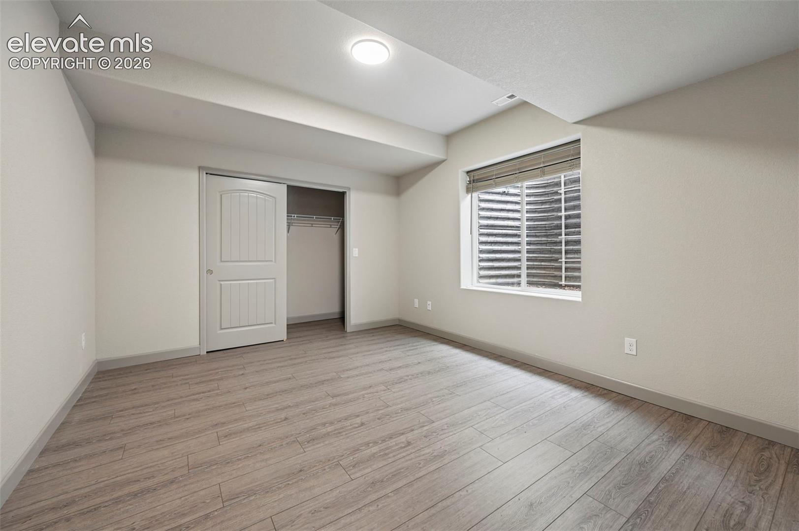 Neutral interior room featuring wood-finish flooring, a recessed window with an egress well, and a closet with a two-panel door