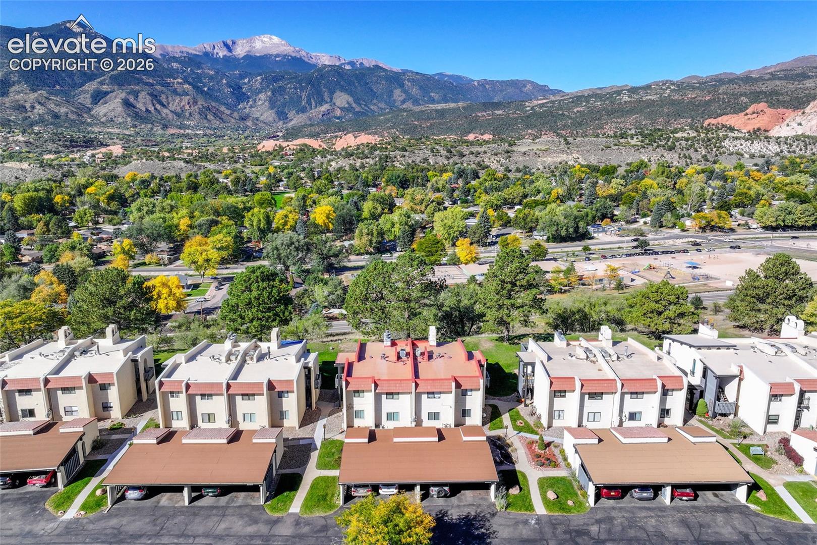 Multi-family residential complex featuring stucco exterior walls, pitched roofing, and individual covered parking structures set against a mountainous backdrop