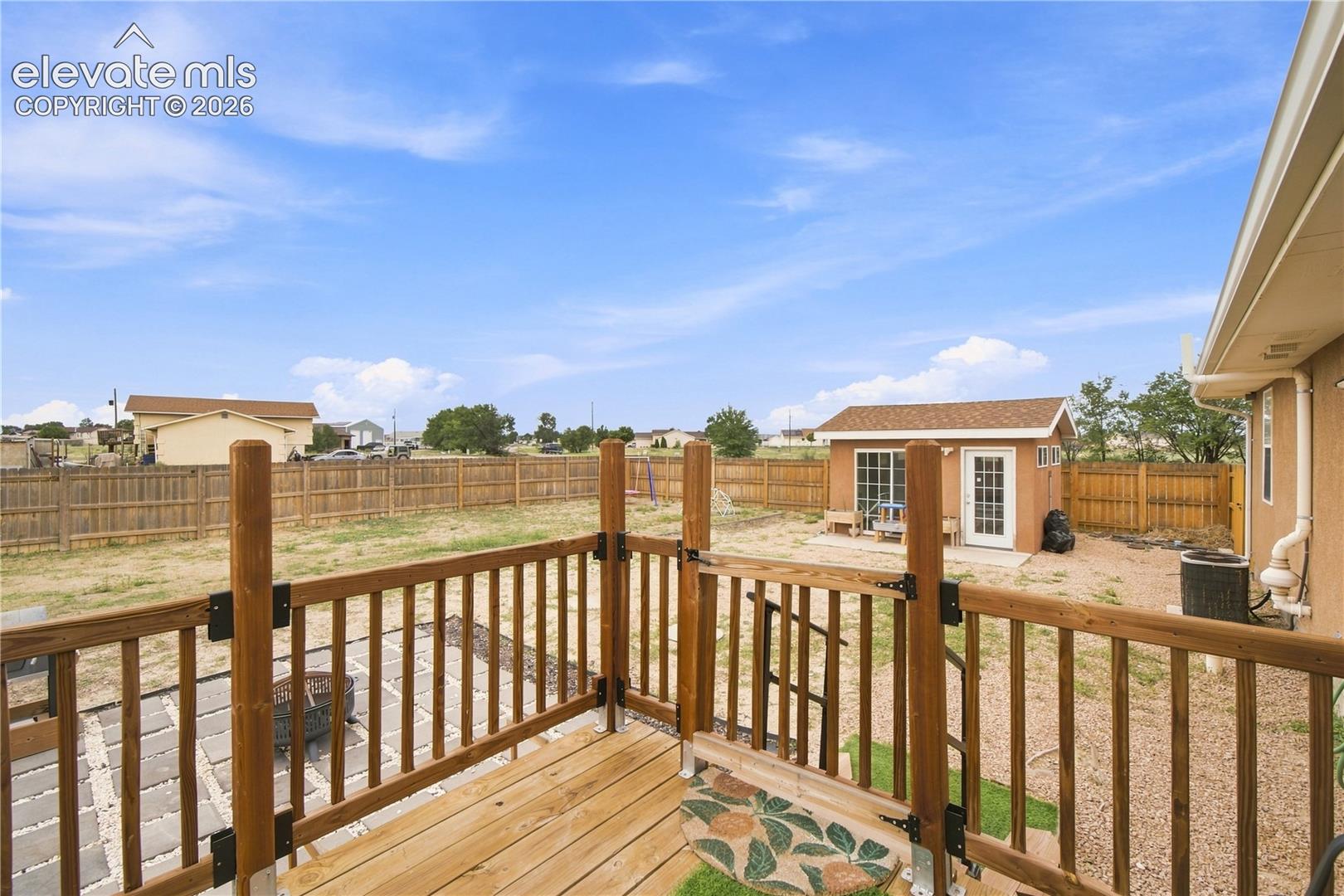 Wood deck with railing, fenced yard, detached shed with exterior lighting, stucco siding, and paved patio area