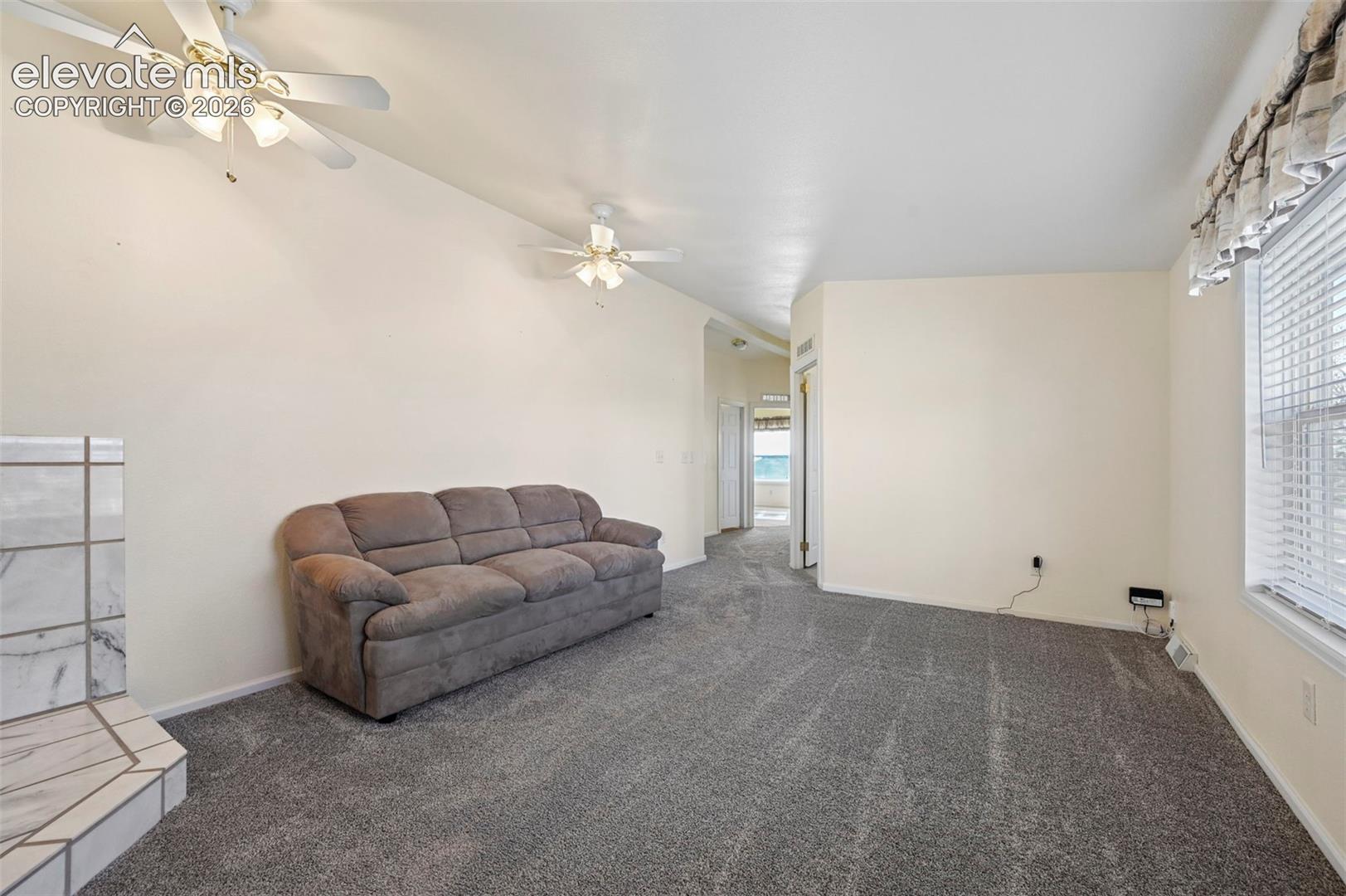 Neutral-toned interior space featuring a stone-faced fireplace hearth, dual ceiling fans with integrated light fixtures, and wall-to-wall carpeting