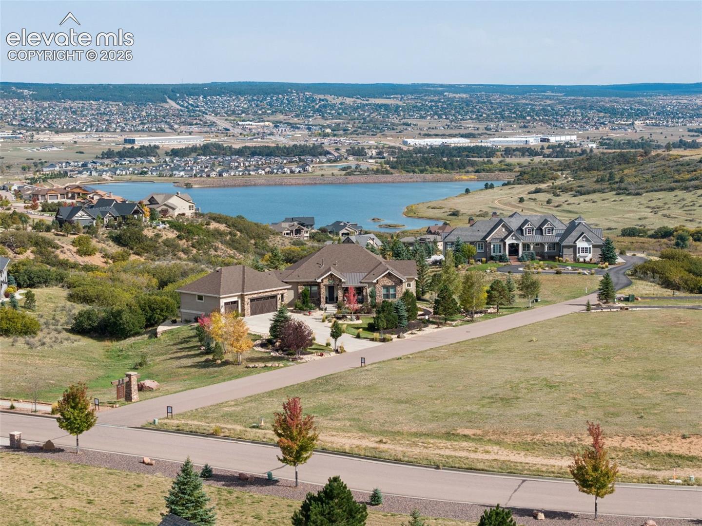Aerial perspective of a multi-structure residence featuring stone and composite shingle exterior siding, multi-car garage, expansive lot, and water scenery