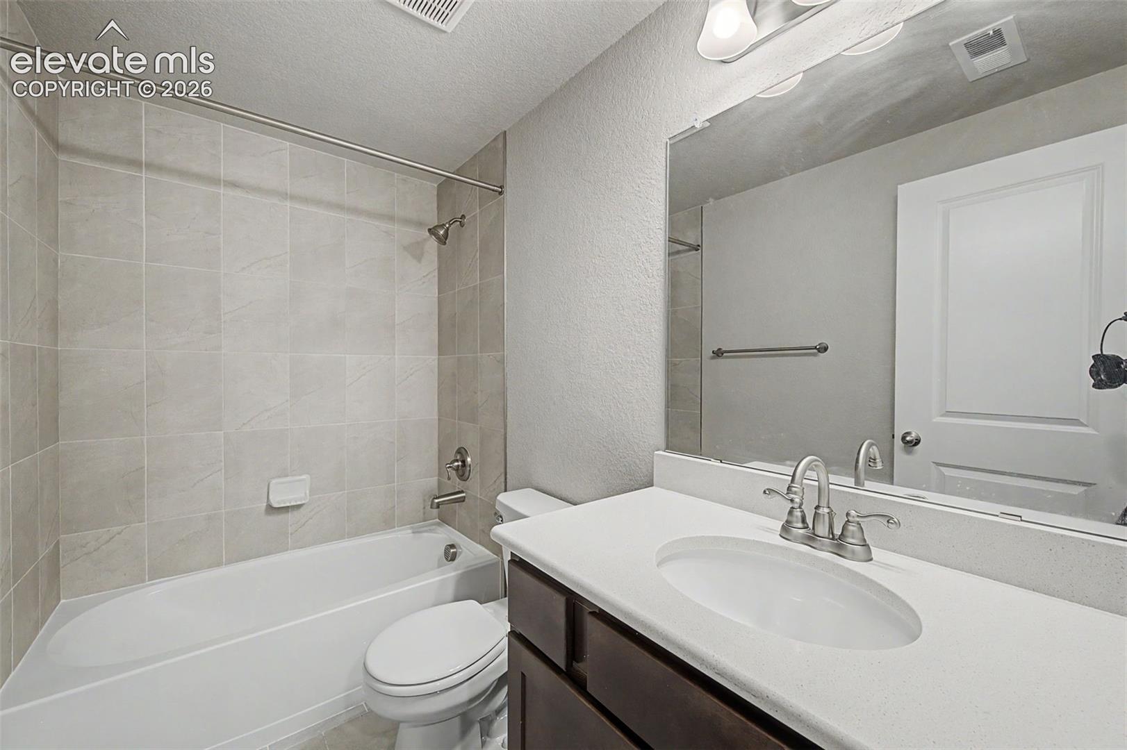 Full bathroom featuring a single vanity with an undermount sink, dark wood-finish cabinetry, and a light-toned countertop