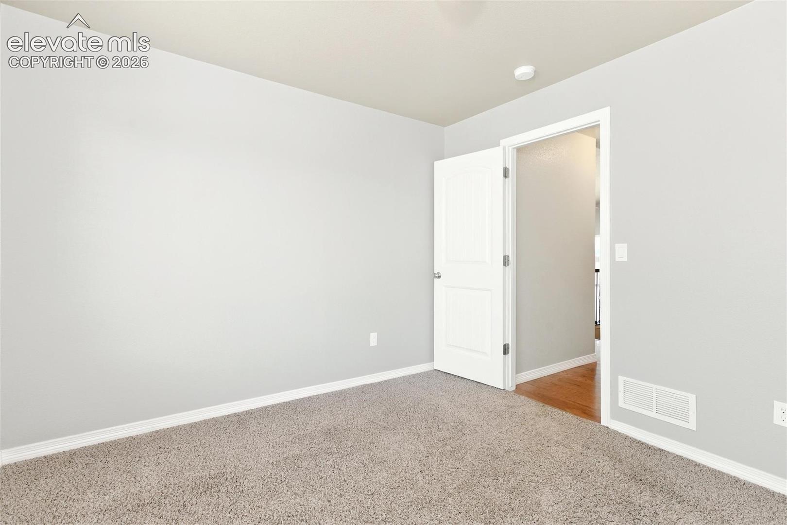 Neutral-toned interior room featuring wall-to-wall carpeting and a white two-panel interior door