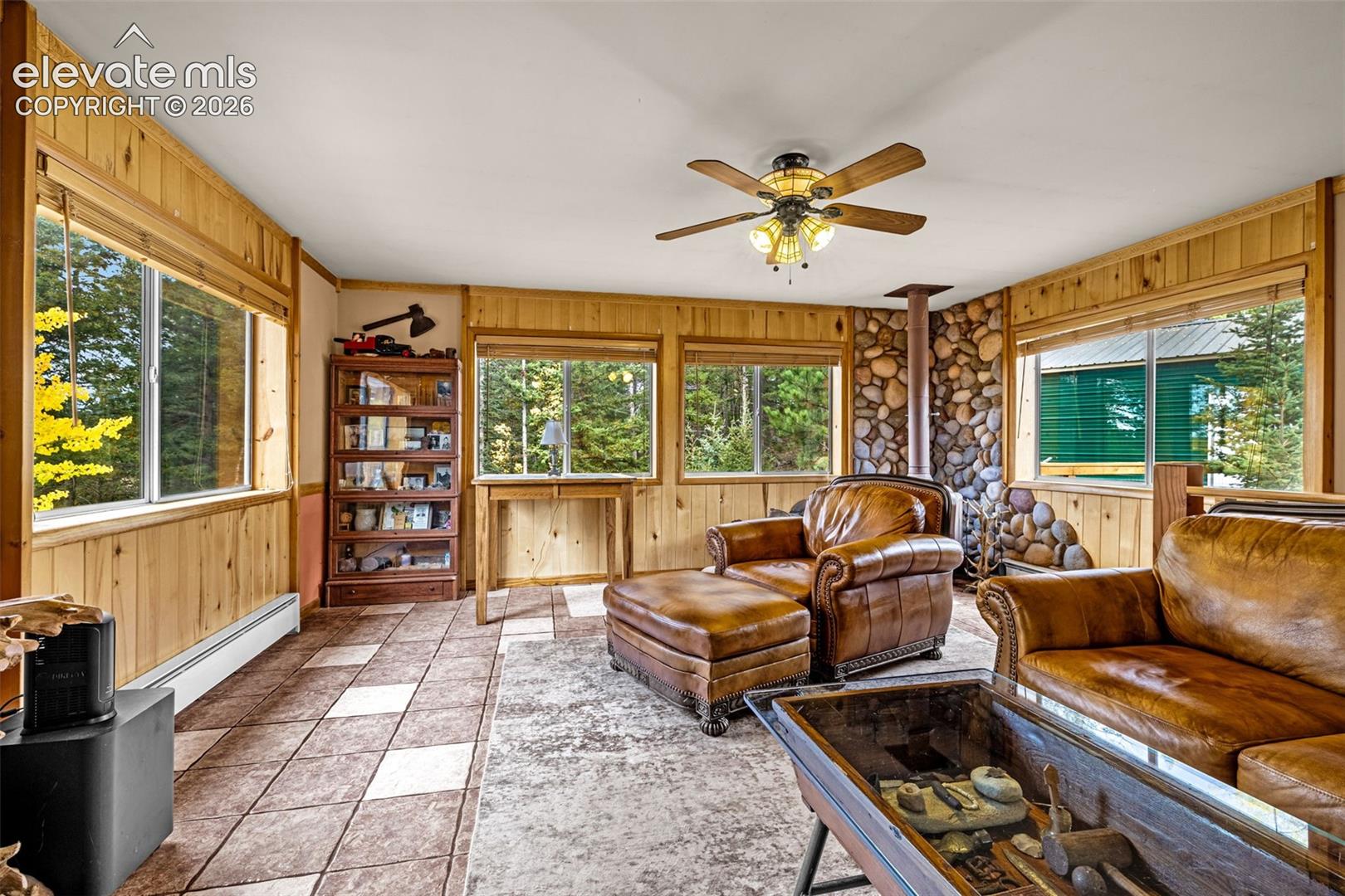 Living area featuring tongue-and-groove wood wall paneling, natural stone fireplace surround, tile flooring, and a ceiling fan with integrated lighting