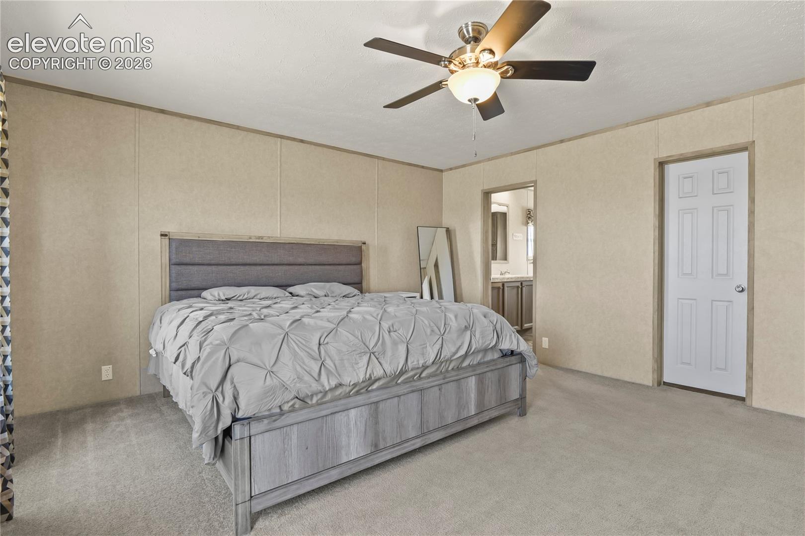 Neutral wall paneling, carpeting, and a ceiling-mounted fan with integrated light fixture, featuring a six-panel door