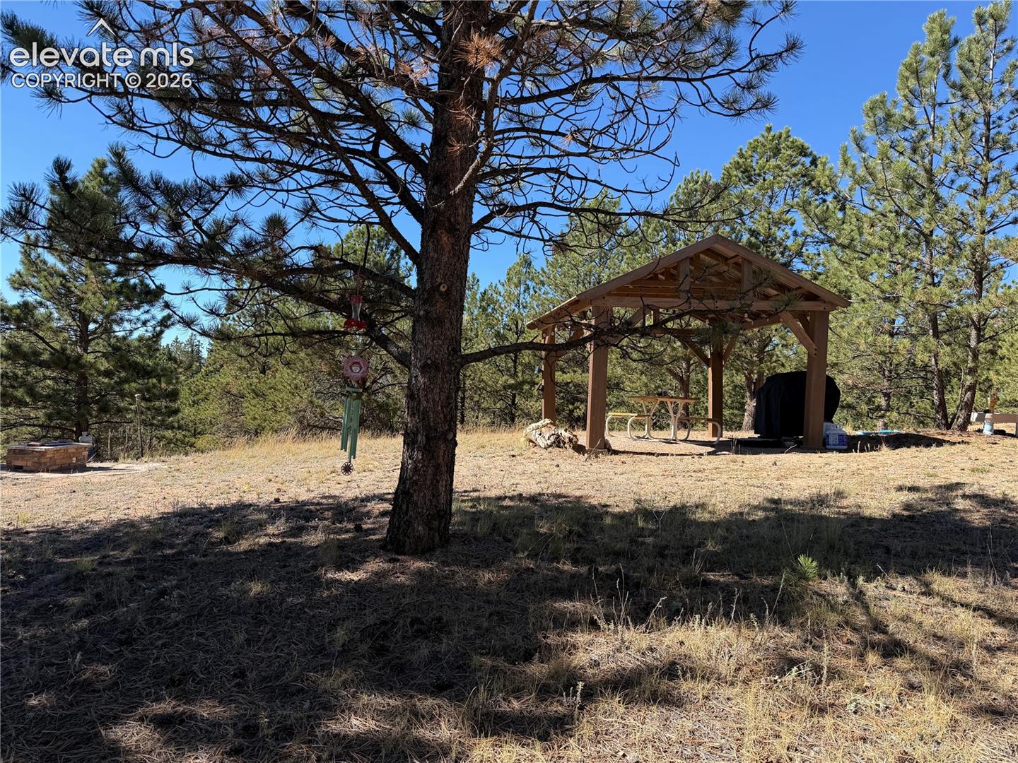 Outdoor area featuring a timber-frame pavilion, stone fire pit, and mature evergreen trees