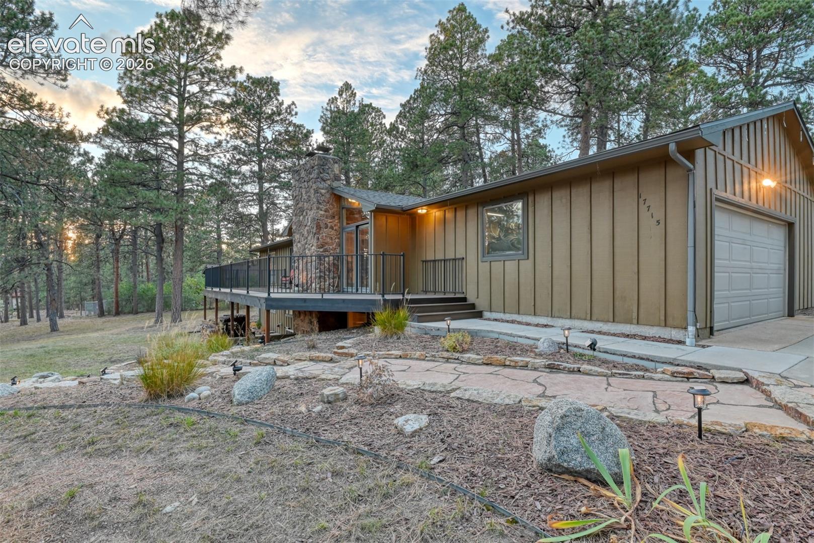 Vertical wood siding exterior featuring a natural stone chimney, an elevated deck with metal railing, and a stone-paver walkway