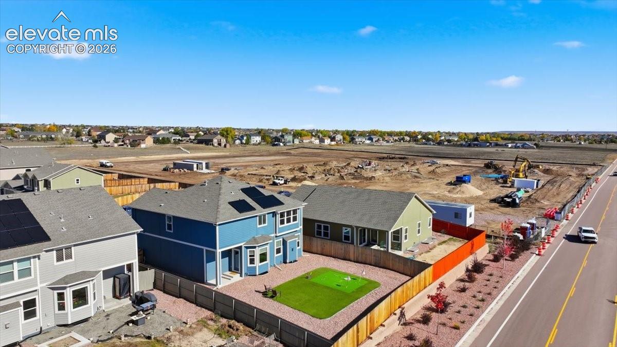 Aerial perspective featuring a two-story residence with rooftop solar panels, a fenced backyard, and a built-in putting green