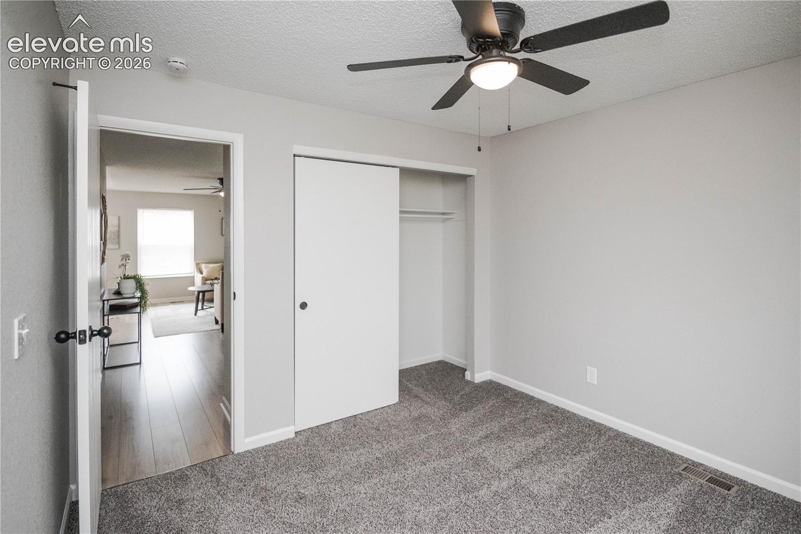 Neutral-toned interior featuring wall-to-wall carpeting, a ceiling fan with integrated lighting, and a closet with sliding doors