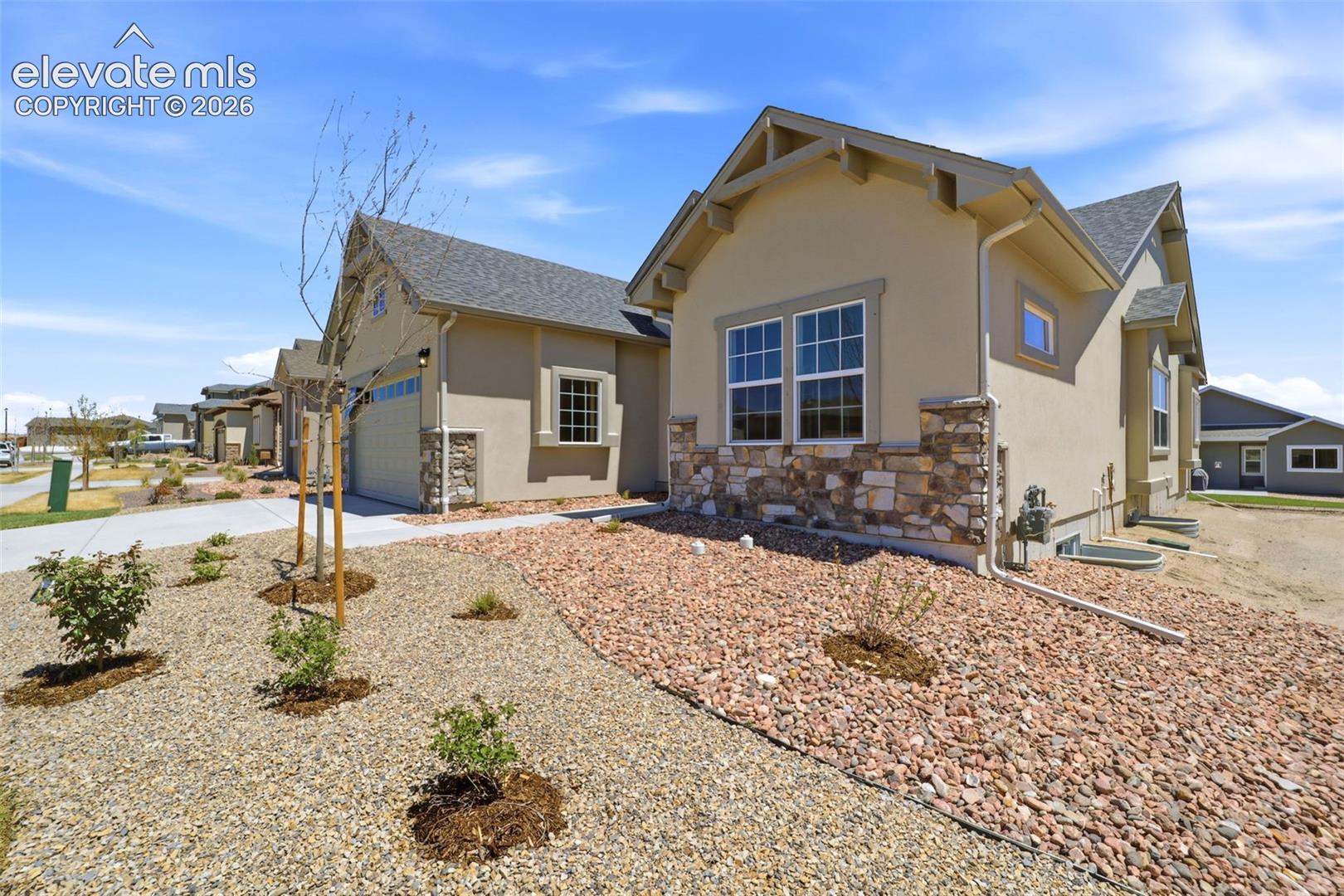 Single-story exterior featuring a stucco façade, decorative stone veneer accents, multi-gabled roofline, and attached garage with a concrete driveway