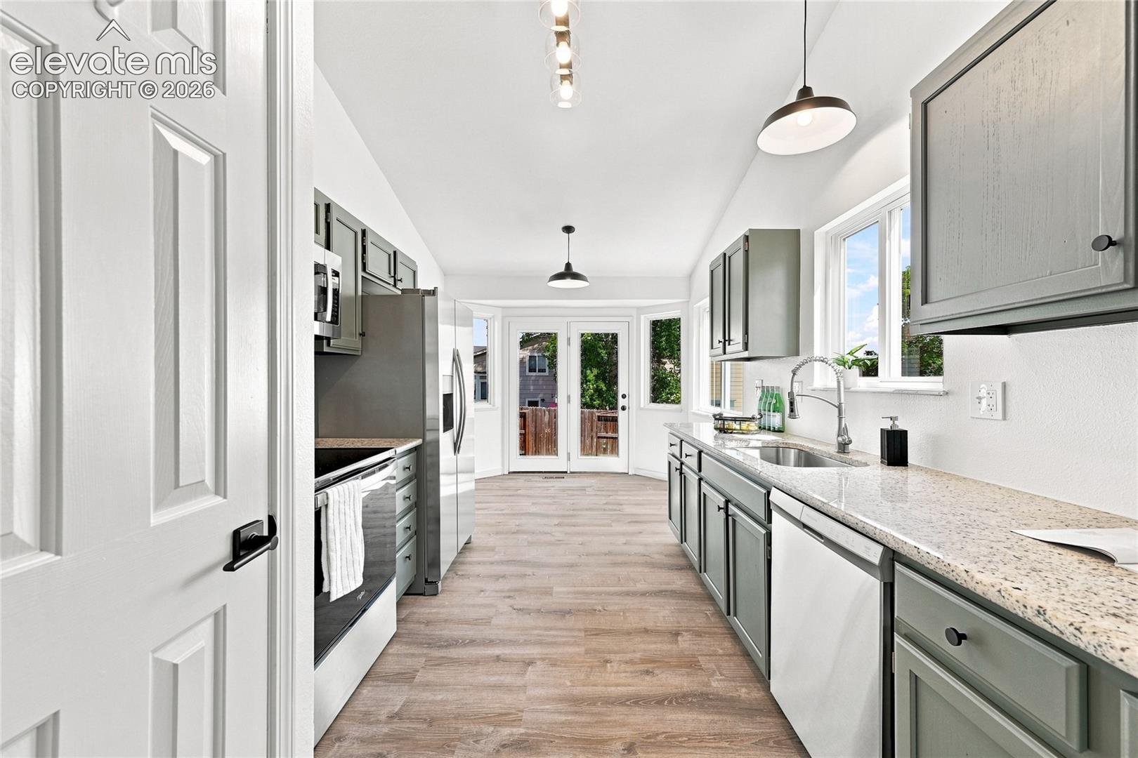 Galley kitchen with wood-finish flooring, gray cabinetry, stainless steel appliances, granite countertops, and rear French doors