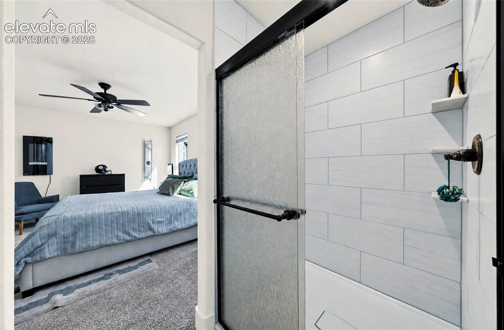 Shower enclosure featuring horizontal light-toned tile, built-in shelving, a glass door with a matte black frame, and a wall-mounted fixture
