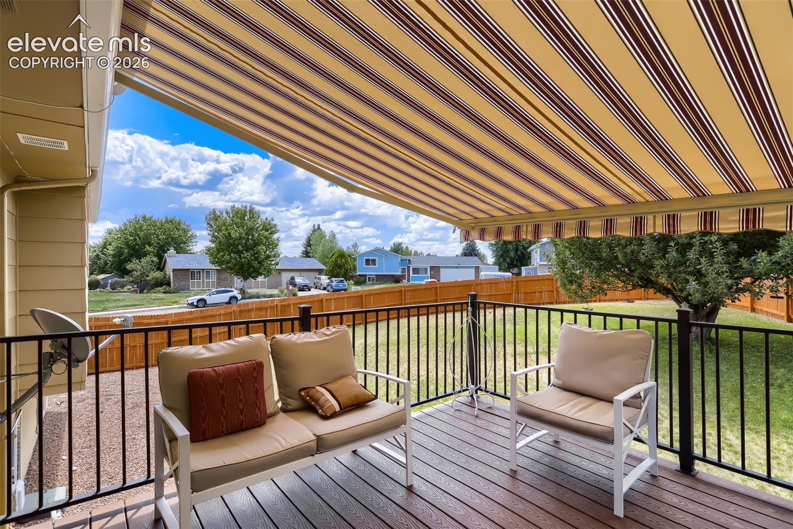 Spacious outdoor deck featuring an extendable striped awning, dark composite decking, and black metal railings, overlooking a fenced yard