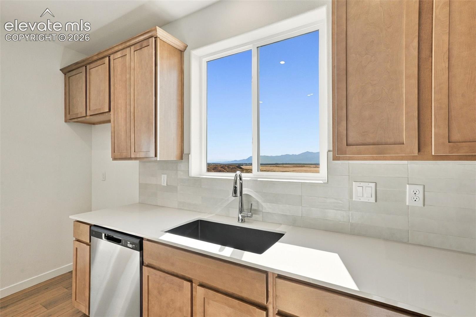 Kitchen featuring wood cabinetry, light-toned countertops, a stainless-steel dishwasher, a black undermount sink with a chrome faucet, and a large window